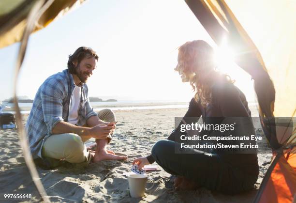 couple camping playing cards on beach at sunset - cream coloured suit 個照片及圖片檔
