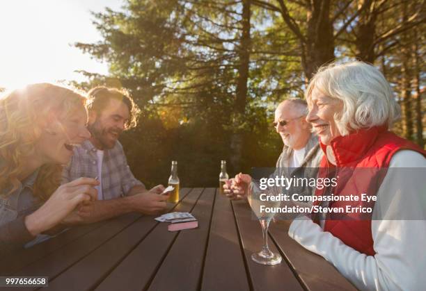 senior couple and adult children playing cards at campsite picnic table - "compassionate eye" fotografías e imágenes de stock