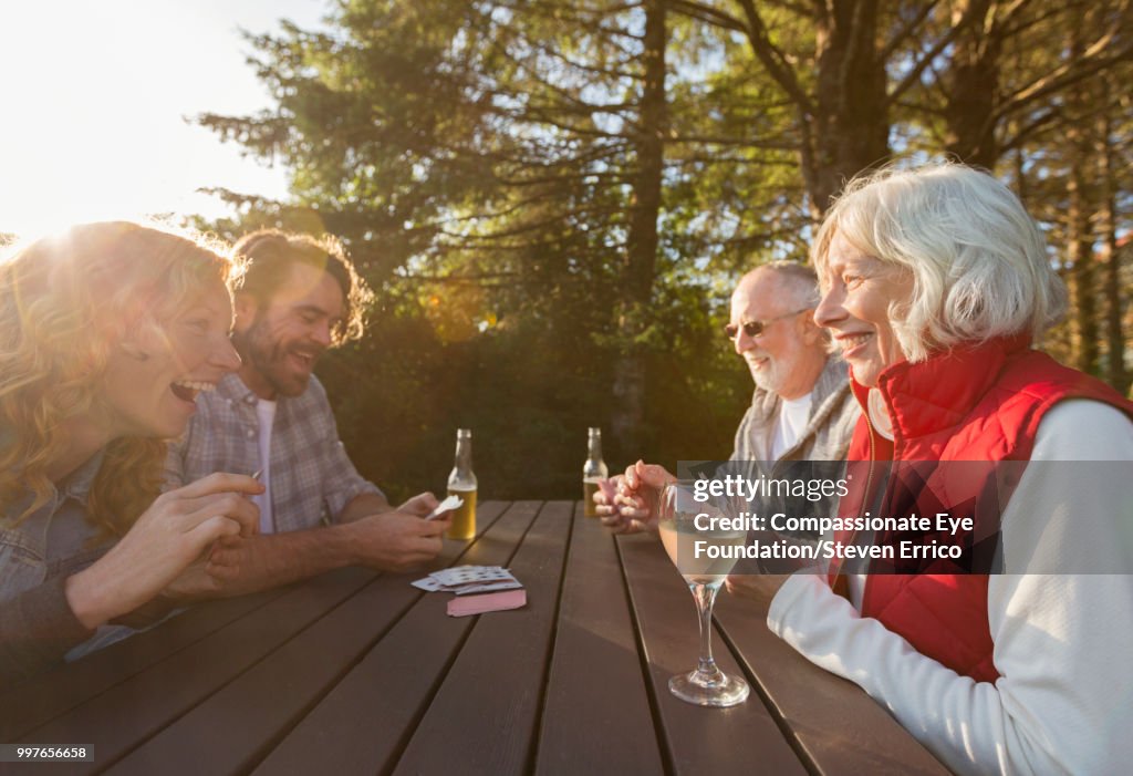 Senior couple and adult children playing cards at campsite picnic table