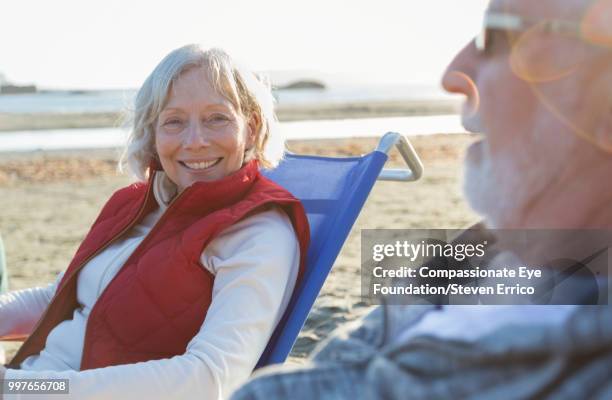senior couple relaxing on beach at sunset - "compassionate eye" fotografías e imágenes de stock