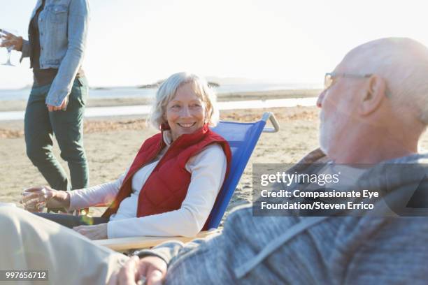 senior couple and family relaxing on beach at sunset - compassionate eye foundation stock-fotos und bilder