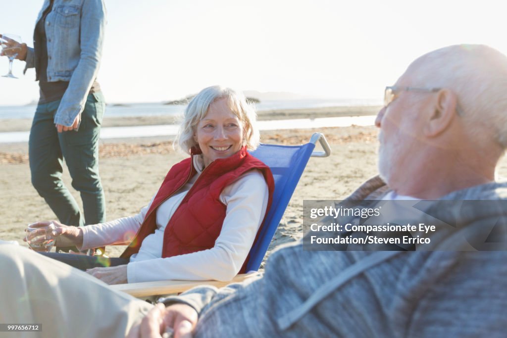 Senior couple and family relaxing on beach at sunset