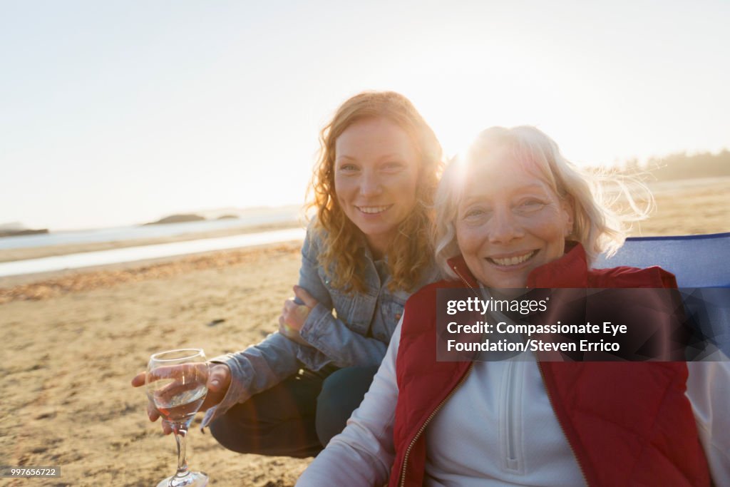 Senior woman and adult daughter relaxing on beach at sunset