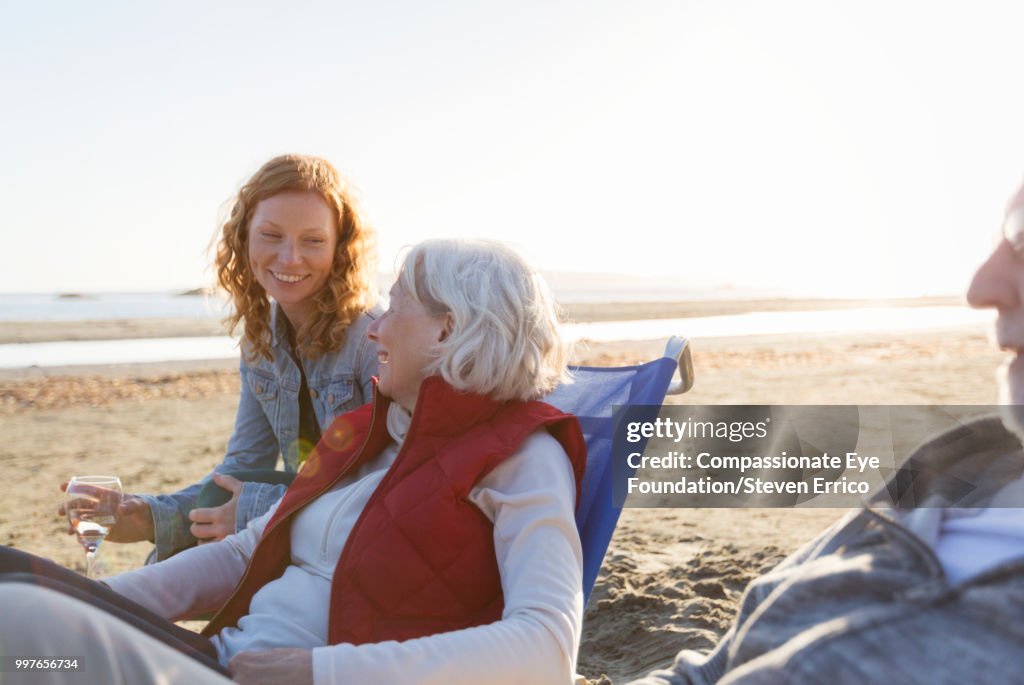 Senior couple and adult daughter relaxing on beach at sunset
