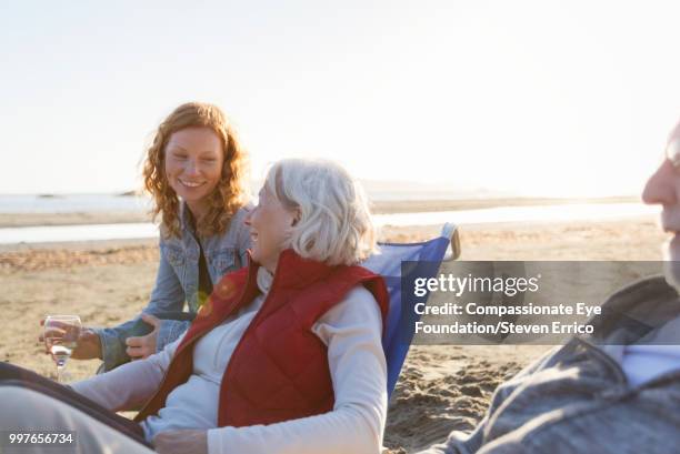 senior couple and adult daughter relaxing on beach at sunset - compassionate eye foundation stockfoto's en -beelden