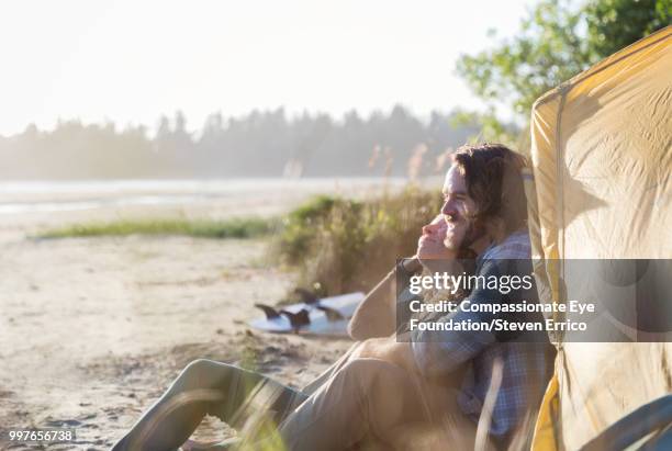 couple sitting on beach looking at ocean view - compassionate eye foundation stockfoto's en -beelden