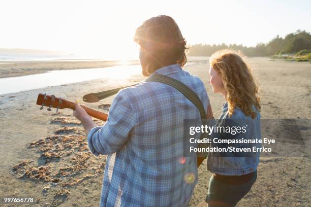 couple playing guitar on beach at sunset - compassionate eye foundation stock-fotos und bilder