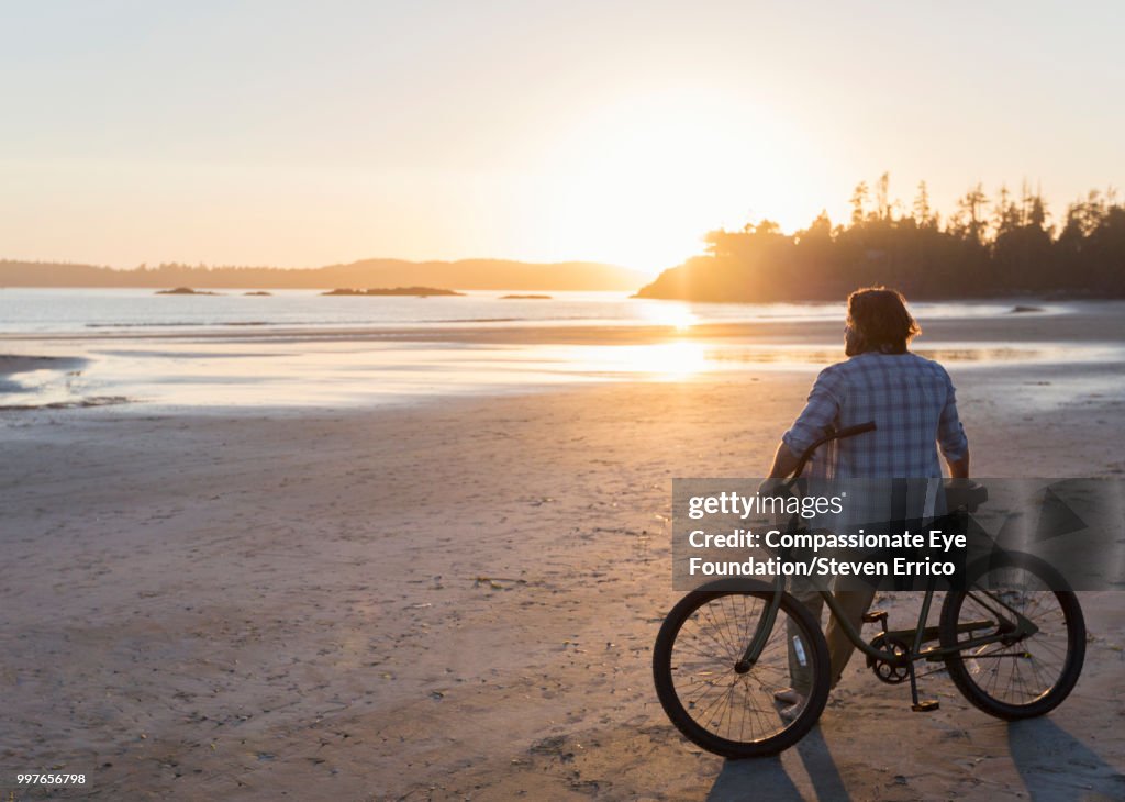 Man siting on bike looking at ocean view at sunset