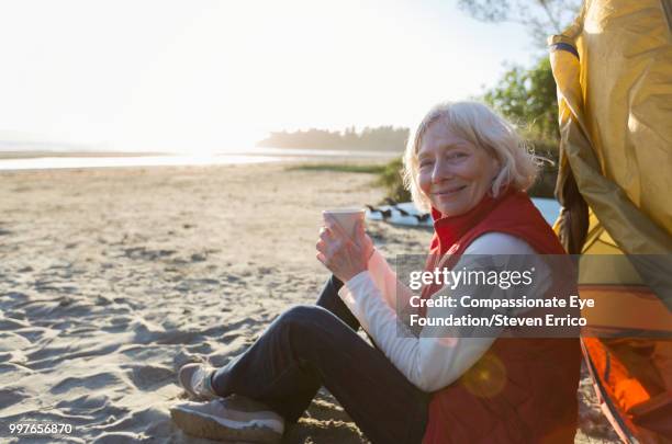 senior woman camping on beach with coffee - "compassionate eye" fotografías e imágenes de stock