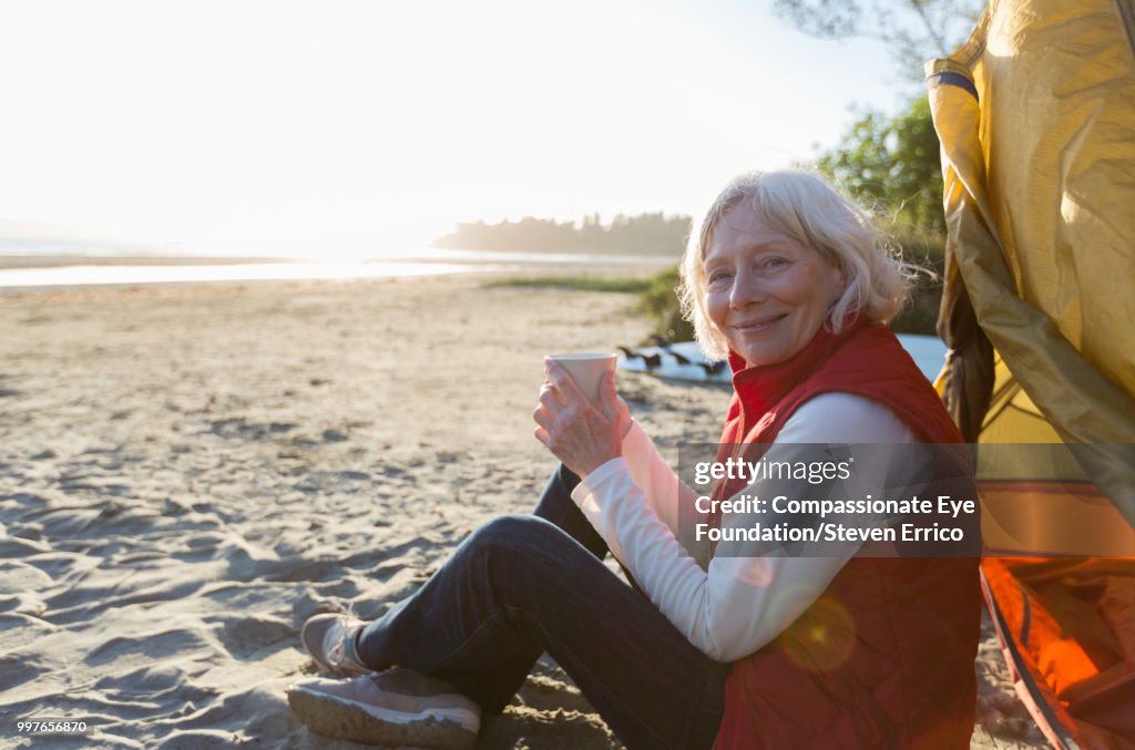 Senior woman camping on beach with coffee