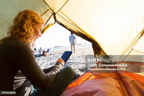 woman camping using smart phone on beach at sunset - cef do not delete stock pictures, royalty-free photos & images