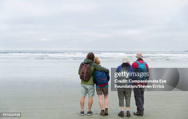 senior couple and adult children hiking on beach looking at ocean view - compassionate eye foundation stock-fotos und bilder