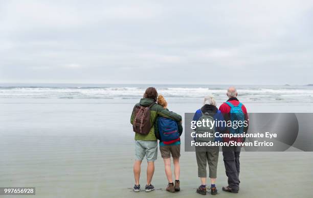 senior couple and adult children hiking on beach looking at ocean view - "compassionate eye" fotografías e imágenes de stock