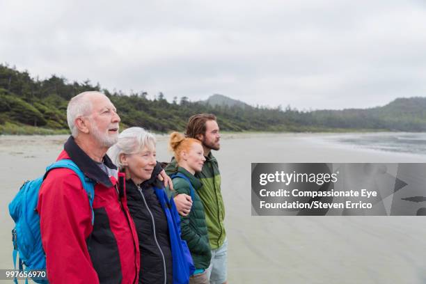 senior couple and adult children hiking on beach looking at ocean view - "compassionate eye" fotografías e imágenes de stock