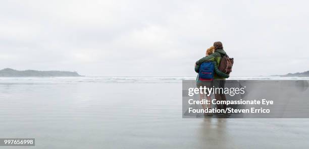 couple hiking on beach looking at ocean view - "compassionate eye" fotografías e imágenes de stock