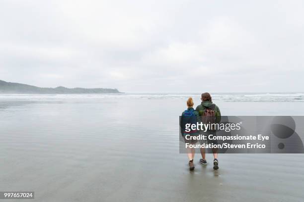 couple hiking on beach - compassionate eye stockfoto's en -beelden