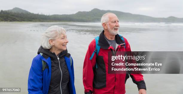 senior couple hiking on beach - "compassionate eye" fotografías e imágenes de stock