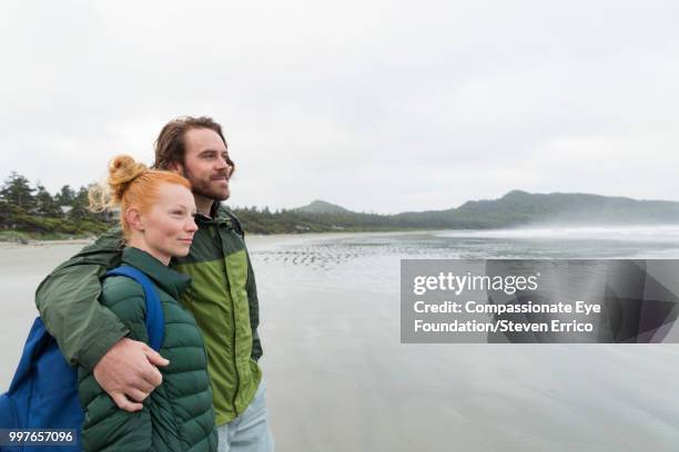 couple hiking on beach looking at ocean view - "compassionate eye" fotografías e imágenes de stock