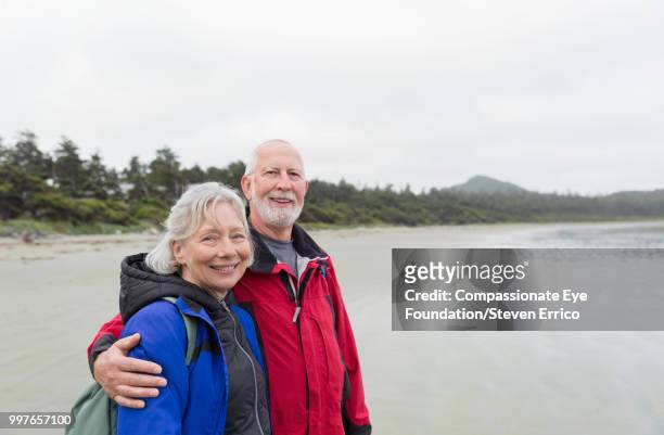 portrait of senior couple hiking on beach - compassionate eye foundation stock-fotos und bilder