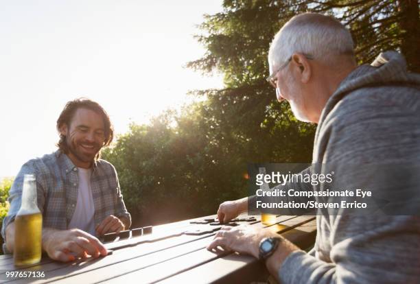 senior man and adult son playing dominoes at campsite picnic table - "compassionate eye" fotografías e imágenes de stock