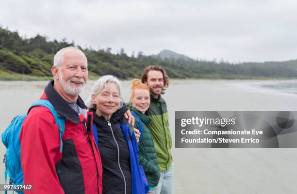 senior couple and adult children hiking on beach looking at ocean view - compassionate eye foundation stock-fotos und bilder