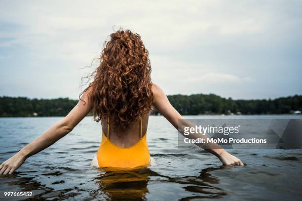 young woman wading in water at lake - curly hair back stock pictures, royalty-free photos & images