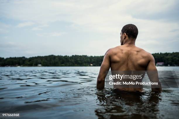young man wading in water at lake - hüfttief im wasser stock-fotos und bilder