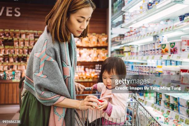 pretty young mom shopping for dairy products joyfully with her lovely baby in the shopping cart. - baby products stock pictures, royalty-free photos & images