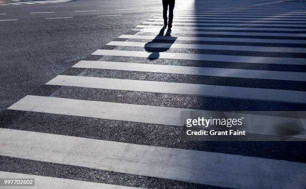 man walking across large intersection. - crossing stock pictures, royalty-free photos & images