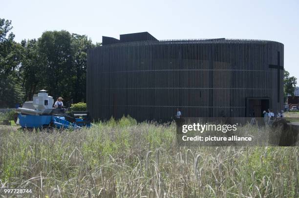 Farmer operates a small combine harvester in a field of rye near the Chapel of Reconciliation on the grounds of the Bernauer Street memorial site in...