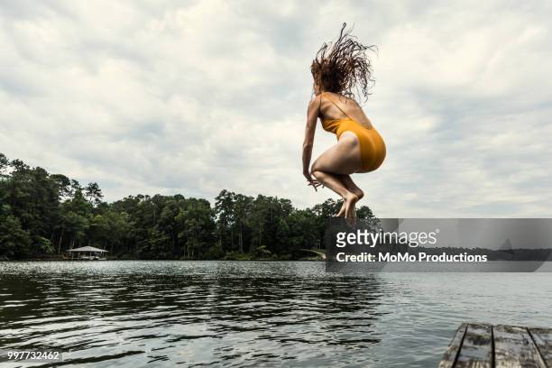 young woman jumping off dock into lake - jumping into lake stock pictures, royalty-free photos & images