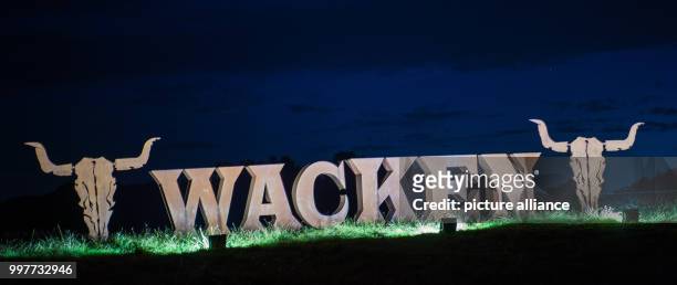 Floodlights shining their lights on the logo of the Wacken Open Air festival, which is made of one-meter high metal letters placed on a lawn at the...