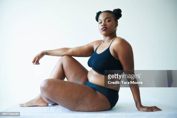 confident curvy woman sitting and looking to camera - curvy black women stockfoto's en -beelden