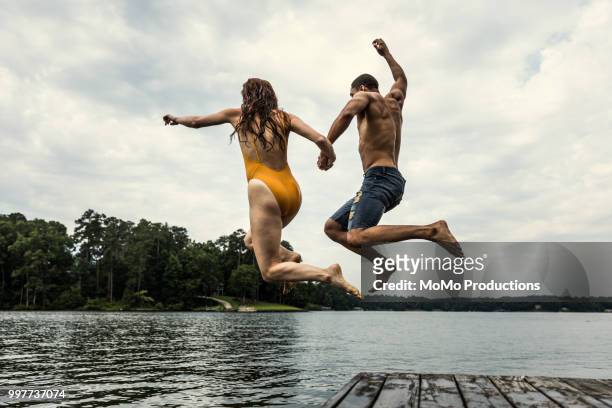 young couple jumping off dock into lake - black shorts photos et images de collection
