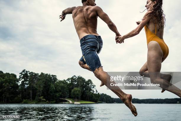 young couple jumping off dock into lake - jumping into water stock-fotos und bilder