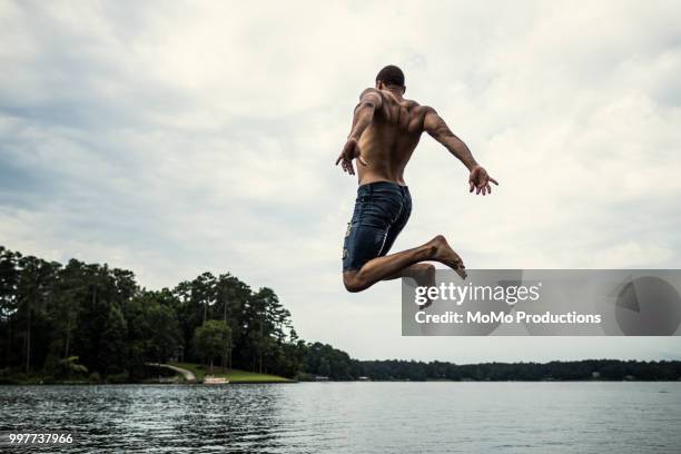 young man jumping off dock into lake - jumping into water stock pictures, royalty-free photos & images