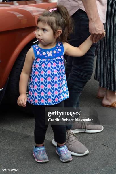 Young girl with a sucker or lollipop in her mouth holds hands with her father at a Fourth of July holiday event in Santa Fe, New Mexico.