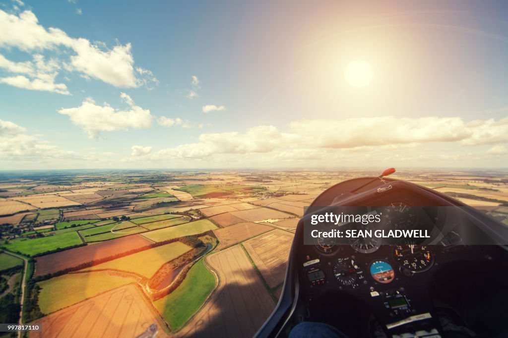 Flying glider aircraft over farmland with sun in sky