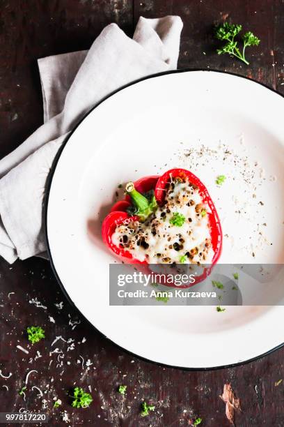 top view of baked in the oven red bell pepper stuffed with minced pork and beef meat, covered with melted cheese, served with fresh parsley in a plate on a wooden table. comfort food. picnic food. - roasted pepper stock-fotos und bilder