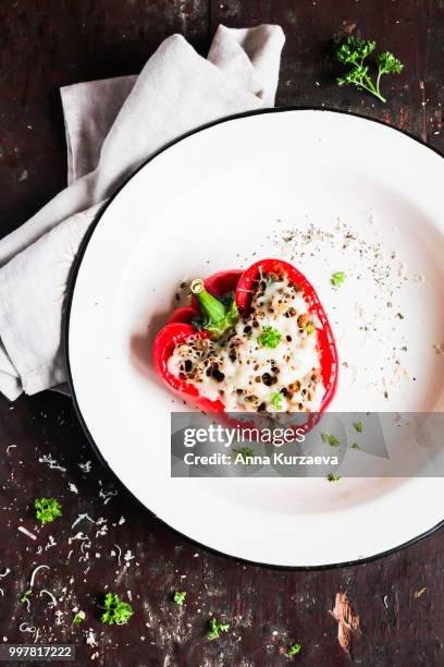 top view of baked in the oven red bell pepper stuffed with minced pork and beef meat, covered with melted cheese, served with fresh parsley in a plate on a wooden table. comfort food. picnic food. - geroosterde rode paprika stockfoto's en -beelden
