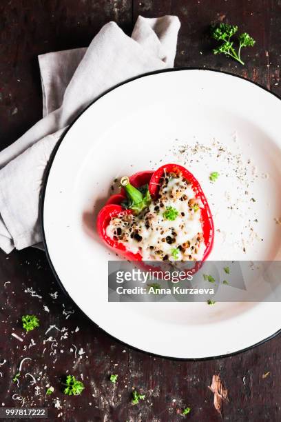 top view of baked in the oven red bell pepper stuffed with minced pork and beef meat, covered with melted cheese, served with fresh parsley in a plate on a wooden table. comfort food. picnic food. - pimentão vermelho assado - fotografias e filmes do acervo