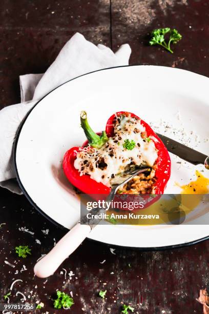 top view of baked in the oven red bell pepper stuffed with minced pork and beef meat, covered with melted cheese, served with fresh parsley in a plate on a wooden table. comfort food. picnic food. - roasted pepper stock-fotos und bilder