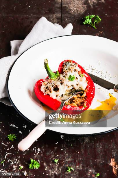 top view of baked in the oven red bell pepper stuffed with minced pork and beef meat, covered with melted cheese, served with fresh parsley in a plate on a wooden table. comfort food. picnic food. - pimentão vermelho assado - fotografias e filmes do acervo