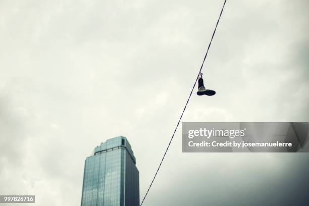 cable con zapatillas colgando frente a un gran edificio azul - josemanuelerre stock-fotos und bilder