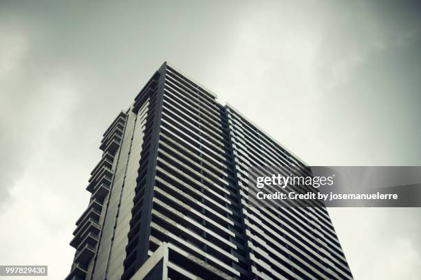 rascacielos. edificio muy alto de cristal y metálico donde se refleja la luz del día sobre un cielo gris con algunas nubes. escena tomada desde abajo. - día stock-fotos und bilder