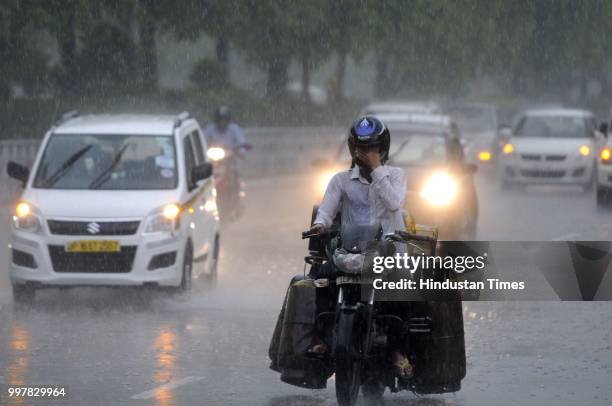 Commuters travel during heavy rainfall near Film City road, on July 13, 2018 in Noida, India. The heavy rains came as a respite to the people of...