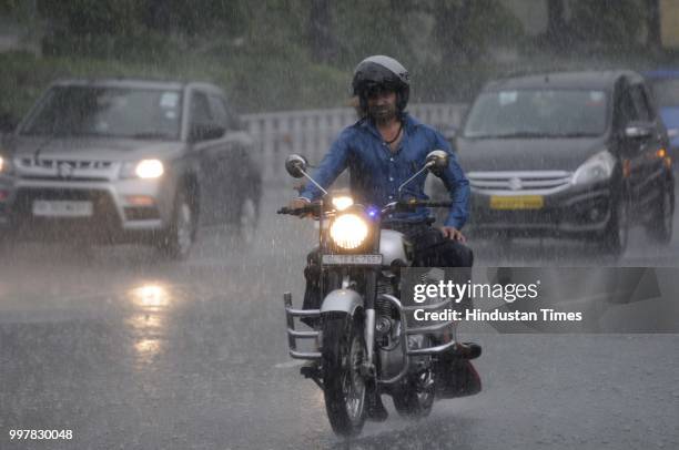 Commuters travel during heavy rainfall near Film City road, on July 13, 2018 in Noida, India. The heavy rains came as a respite to the people of...