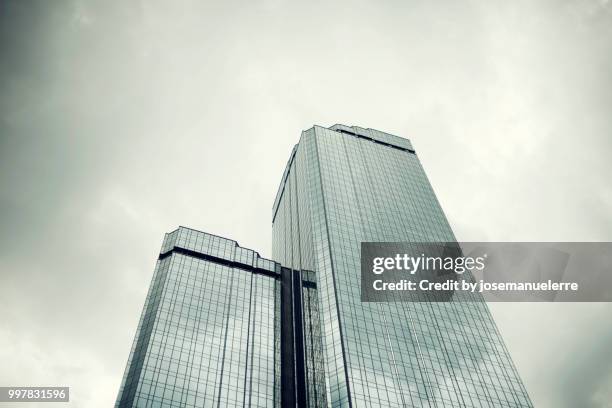 rascacielos. edificio muy alto de cristal y metálico donde se refleja la luz del día sobre un cielo gris con algunas nubes. escena tomada desde abajo. - nubes - fotografias e filmes do acervo