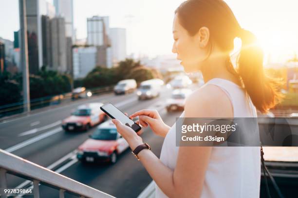 beautiful young woman using mobile app on smart watch to arrange taxi ride in busy city street, with blurry traffic scene as background - ���������������������������������������������������������������app���������zg357cc��������������������������������������������������������������� photos et images de collection