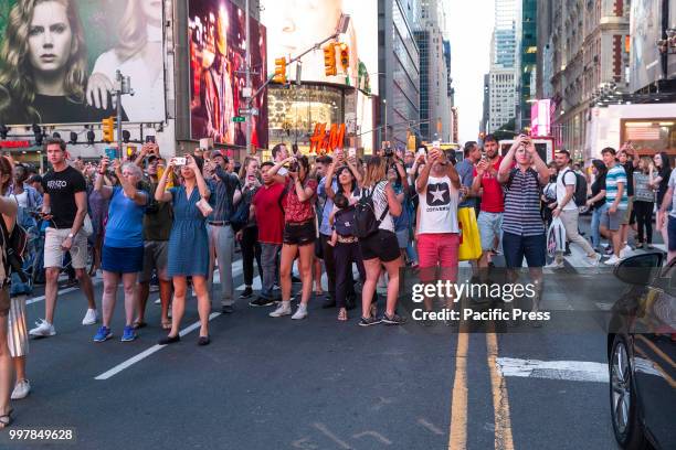 People stand on 42nd Street in Manhattan to photograph Manhattanhenge phenomenon when sun sets in alignment with streets run East to West.